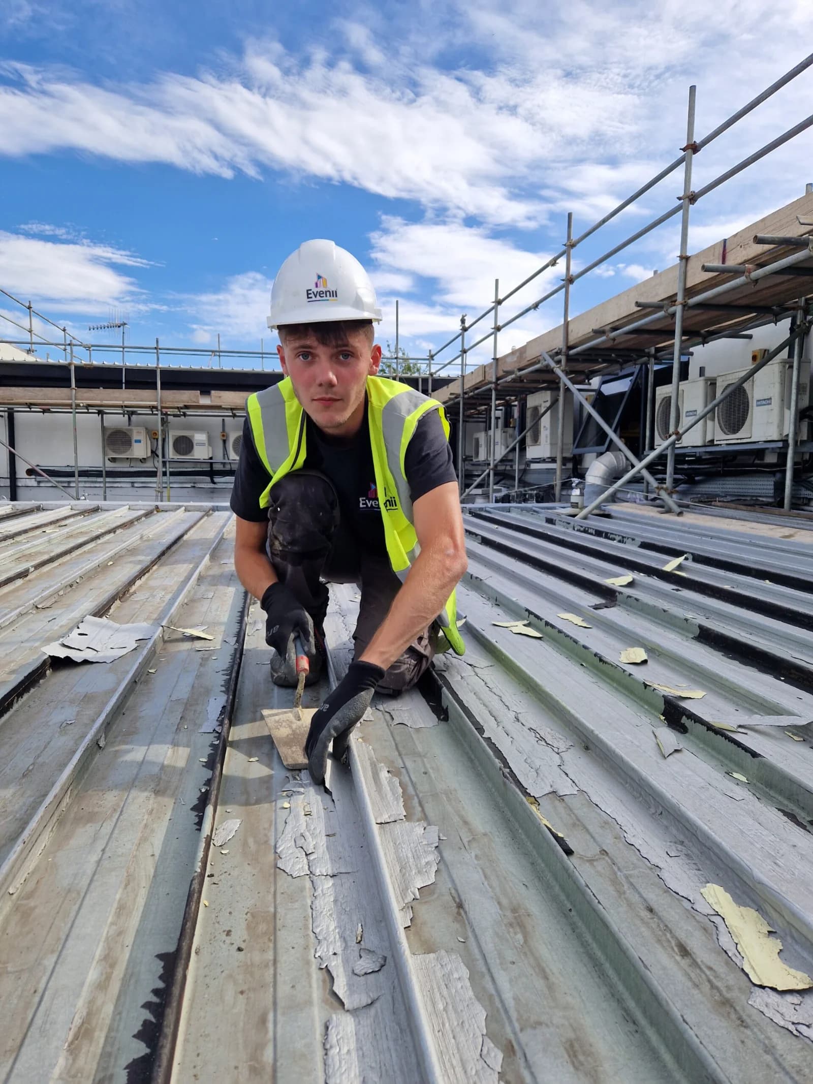 Roofer in branded hi-vis and harness working on a commercial roof in the Northeast